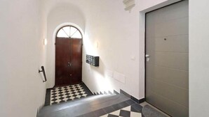 Um corredor com piso xadrez, uma porta de madeira com painel de vidro e uma porta cinza.