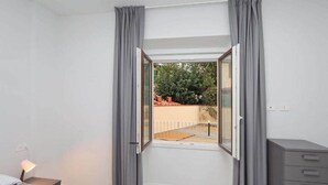 Quarto com uma janela grande, uma cama, uma mesa de cabeceira e uma cômoda cinza.