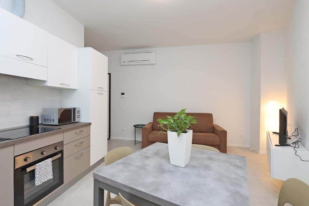 Una cucina funzionale con elettrodomestici moderni, una zona pranzo con tavolo e sedie, e un soggiorno con divano e una pianta.