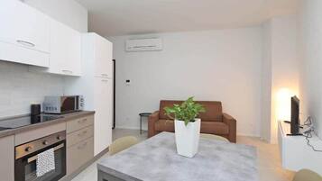Una cucina funzionale con elettrodomestici moderni, una zona pranzo con tavolo e sedie, e un soggiorno con divano e una pianta.