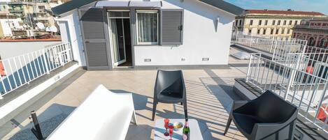 Une terrasse sur le toit avec une baignoire blanche, deux chaises noires et une petite table sur laquelle se trouvent une bouteille et des verres.