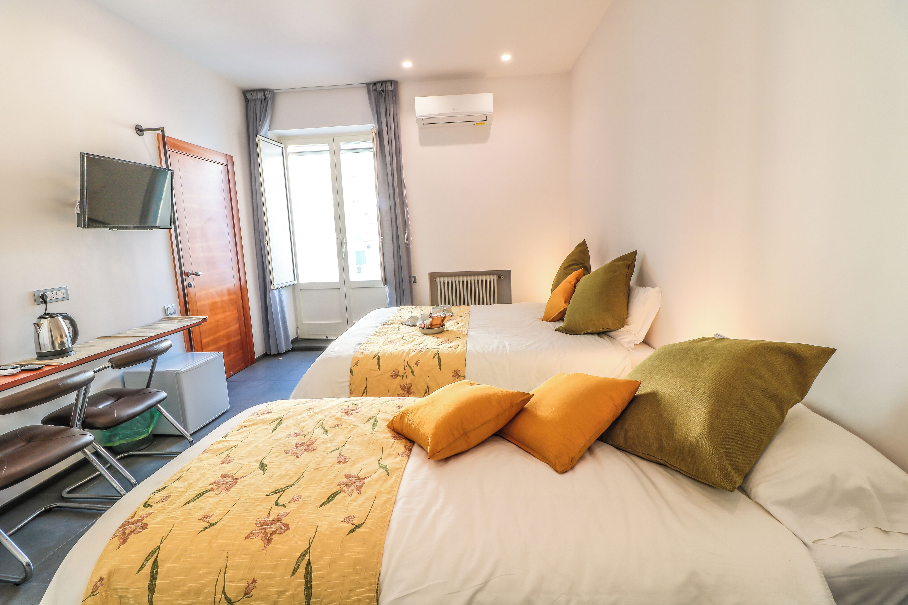 Una habitación de hotel con dos camas, un escritorio con silla, televisor y ventana con cortinas.