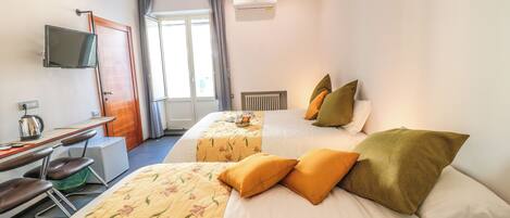 Una habitación de hotel con dos camas, un escritorio con silla, televisor y ventana con cortinas.