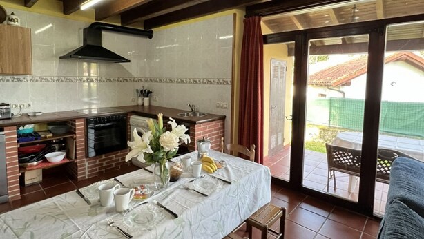 A kitchen with a dining table set for four, a brick oven, and a view of the outdoor patio. - House for 8 Bufones de Pría (Pria)