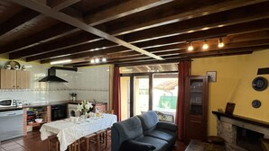 A cozy living room with a sofa and a dining table set for four. A kitchen with modern appliances and a chimney is visible in the background. - House for 8 Bufones de Pría (Pria)