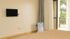 A hotel room with a bed, a television mounted on the wall, a heater, and a view of the outdoors. - Residence Six Sigma (Entebbe)