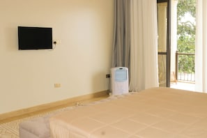 A hotel room with a bed, a television mounted on the wall, a heater, and a view of the outdoors. - Residence Six Sigma (Entebbe)