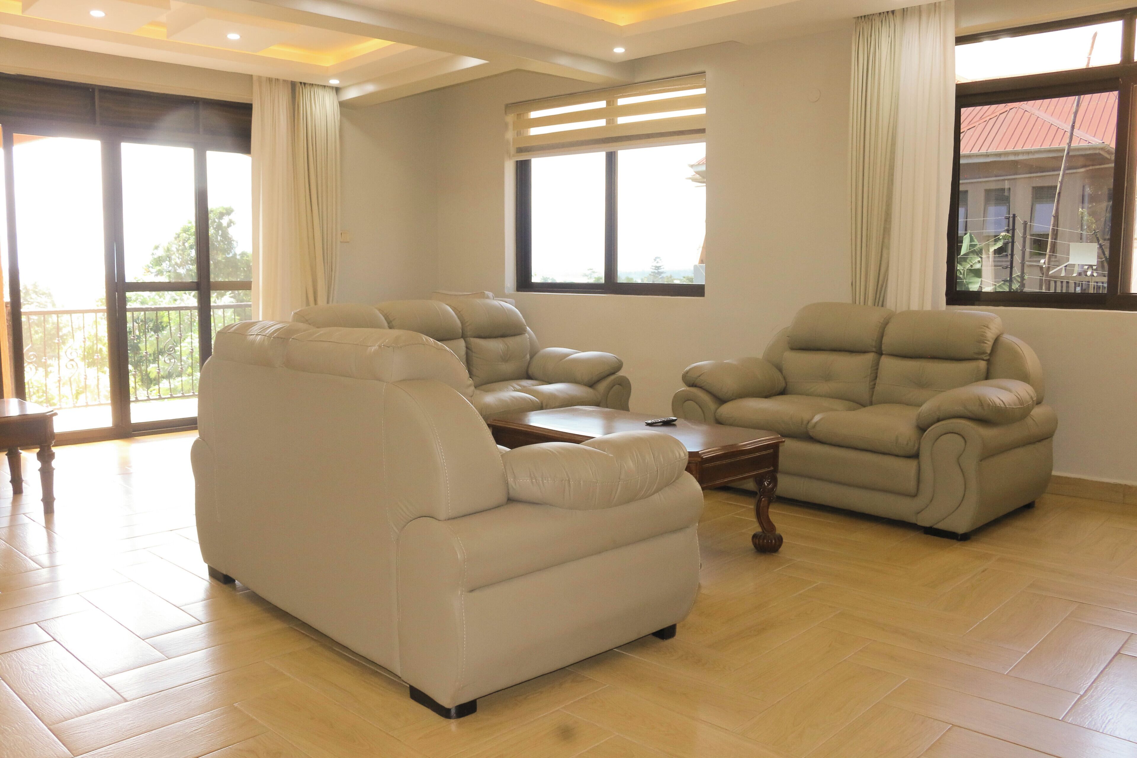 Amplia habitación con dos sofás de cuero, una mesita de madera y ventanas grandes con cortinas.