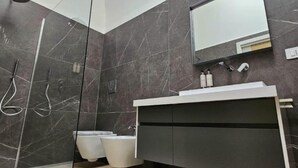 A modern bathroom with dark marble walls, a glass-enclosed shower, a white sink, and a mirror above the vanity. - Luxury Way Drops of Luxury - Exclusive relaxation with whirlpool in Molfetta (Molfetta)
