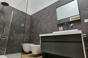 A modern bathroom with dark marble walls, a glass-enclosed shower, a white sink, and a mirror above the vanity. - Luxury Way Drops of Luxury - Exclusive relaxation with whirlpool in Molfetta (Molfetta)