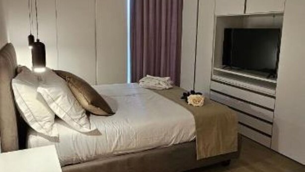 A modern bedroom with a bed, a TV mounted on the wall, and a window with curtains. - Luxury Way Drops of Luxury - Exclusive relaxation with whirlpool in Molfetta (Molfetta)