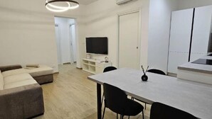 A modern living room with a sofa, a dining table with chairs, a flat-screen TV, and a kitchen area with cabinets. - Luxury Way Drops of Luxury - Exclusive relaxation with whirlpool in Molfetta (Molfetta)