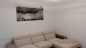 A living room with a beige sofa, a wall-mounted picture of a waterfront scene, and a modern circular light fixture. - Luxury Way Drops of Luxury - Exclusive relaxation with whirlpool in Molfetta (Molfetta)