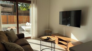 Una sala de estar moderna con un sofá, una mesa de centro, un televisor y un gran ventanal corredizo que da a una zona de estar exterior.
