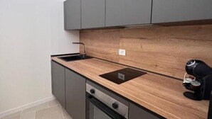 Una cocina moderna con armarios grises, encimera de madera, horno empotrado y una cafetera.
