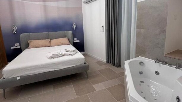 Un dormitorio moderno con cama, un ventanal grande y un baño con bañera.