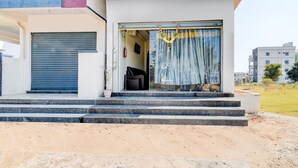 A modern building with a closed blue shutter door, a set of stone steps leading to a glass door with a curtain, and a small garden area in front. - Hotel O Snist University Hyderabad (Hyderabad)