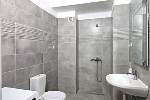 A modern bathroom with grey tiles, a white toilet, a shower with a handheld showerhead, and a sink with a mirror. - Holiday Apartment In Saranda - 003 With Balcony (Sarandë)