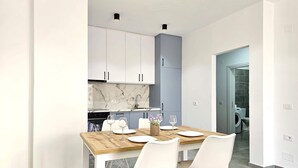 Una cucina moderna con mobili bianchi, una parete di fondo in marmo e un'area pranzo con tavolo in legno e sedie bianche.