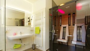 A modern bathroom with a white sink, mirror, and towel rack. There is a glass shower enclosure with two seats and a glass door. - Large apartment in Karlshagen on Usedom with sauna, close to the beach (Karlshagen)