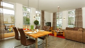 A modern living room with a sofa, a dining table with chairs, and a television. - Large apartment in Karlshagen on Usedom with sauna, close to the beach (Karlshagen)