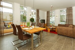 A modern living room with a sofa, a dining table with chairs, and a television. - Large apartment in Karlshagen on Usedom with sauna, close to the beach (Karlshagen)