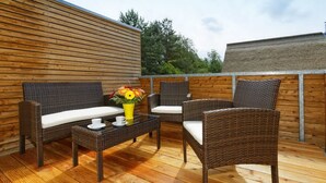A wooden deck with wicker furniture, including a sofa and chairs, and a small table with a yellow vase and a white cup. - Large apartment in Karlshagen on Usedom with sauna, close to the beach (Karlshagen)