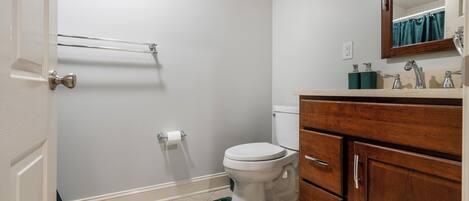 Un baño con inodoro, tocador de madera, espejo y zona de ducha.