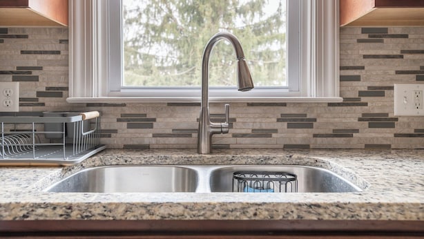 A kitchen with a double sink, a window with a view of trees, and a backsplash with a mosaic tile pattern. - 5 Woods Dr (Mechanicsburg)