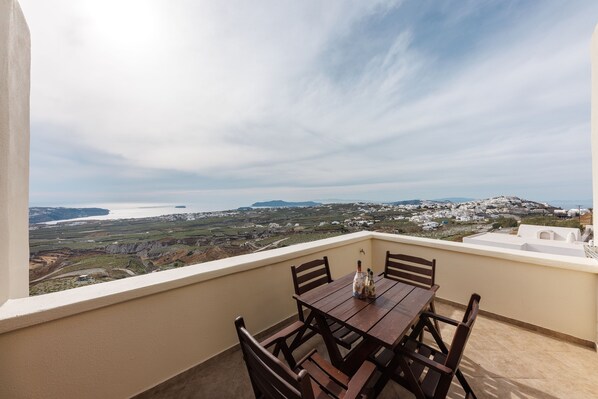 A balcony with a wooden table and chairs, overlooking a coastal landscape with buildings and a body of water. - Apartment - Sleeps 4 - Parking - Sea View (Pyrgos)