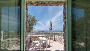 A stone-walled patio with a table and chairs, overlooking a coastal landscape. - Apartment - Sleeps 4 - Parking - Sea View (Pyrgos)