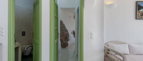 A room with a bed, a green door leading to a bathroom, and a white wall with a picture.