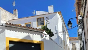A narrow cobblestone street flanked by white buildings with yellow trim and black doors. - Casa Carmo (Évora)