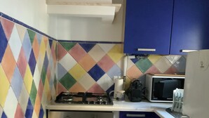A compact kitchen with a gas stove, oven, microwave, and a refrigerator. The walls are tiled with a colorful diamond pattern. - Casa Carmo (Évora)