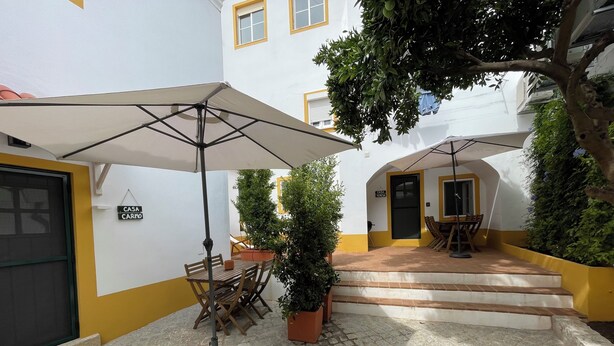 A courtyard with a table and chairs under a large umbrella, a potted plant, and a staircase leading to an entrance. - Casa Carmo (Évora)