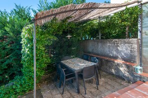Um pátio externo com mesa e cadeiras, luminária pendente e pérgola de tear.