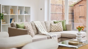 Ein Wohnzimmer mit einem beigefarbenen Sofa, einem Glastisch und einem weißen Bücherregal.