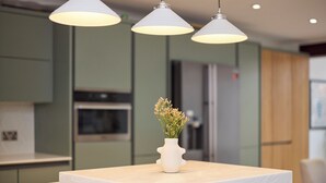Eine Küche mit weißer Arbeitsplatte, einer Blumenvase und drei Pendelleuchten.