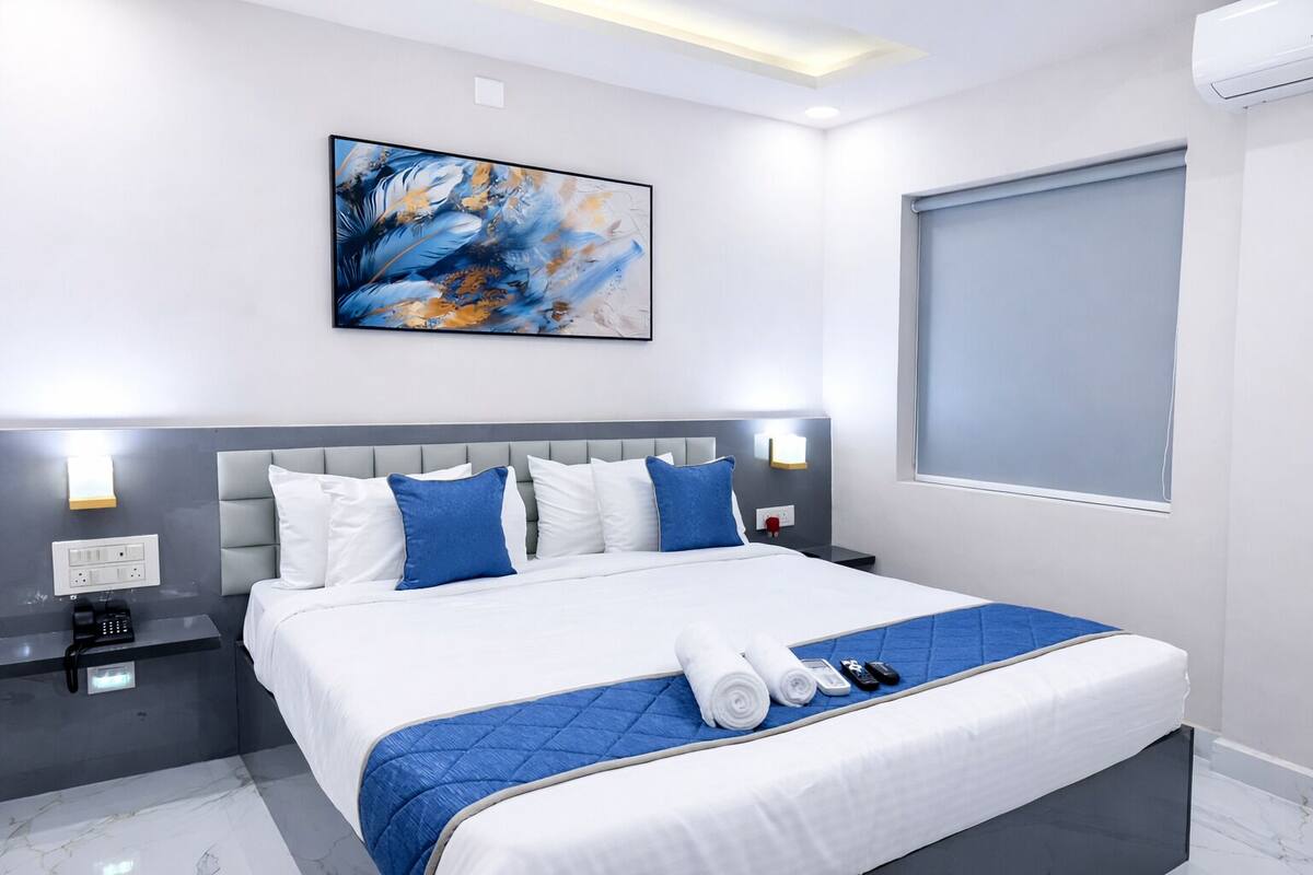 A modern hotel room with a large bed, a headboard, bedside tables, a painting, and a window.