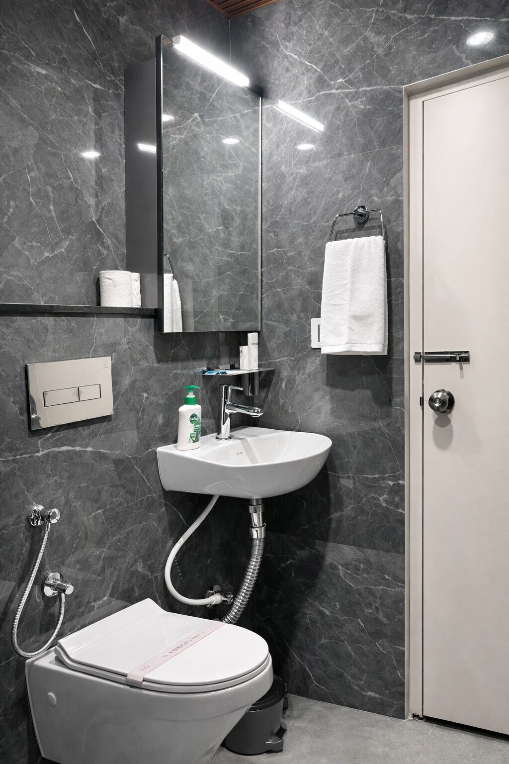 A modern bathroom with a marble wall, a white sink, a toilet, and a door.
