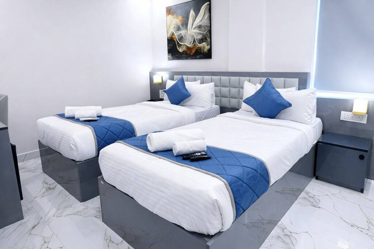 A modern hotel room with two beds, marble flooring, ceiling fans, and an air conditioning unit.