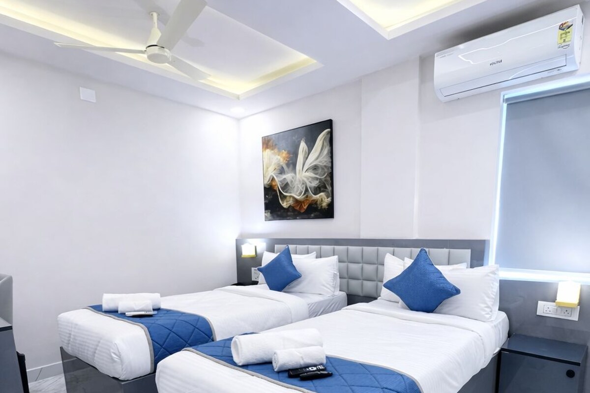 A modern hotel room with two beds, marble flooring, ceiling fans, and an air conditioning unit.