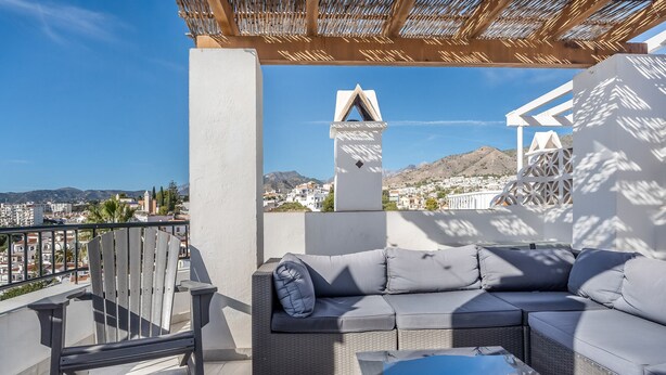 Un balcon avec un canapé en osier, une chaise et une table basse en verre.