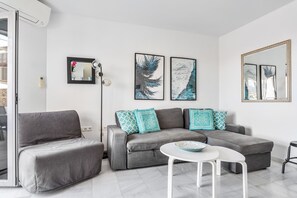 A modern living room with a grey sofa, a smaller grey armchair, and a white coffee table. There are two framed artworks on the wall and a large mirror. - Sea View Home with 3 Terraces near Burriana Beach (Nerja)