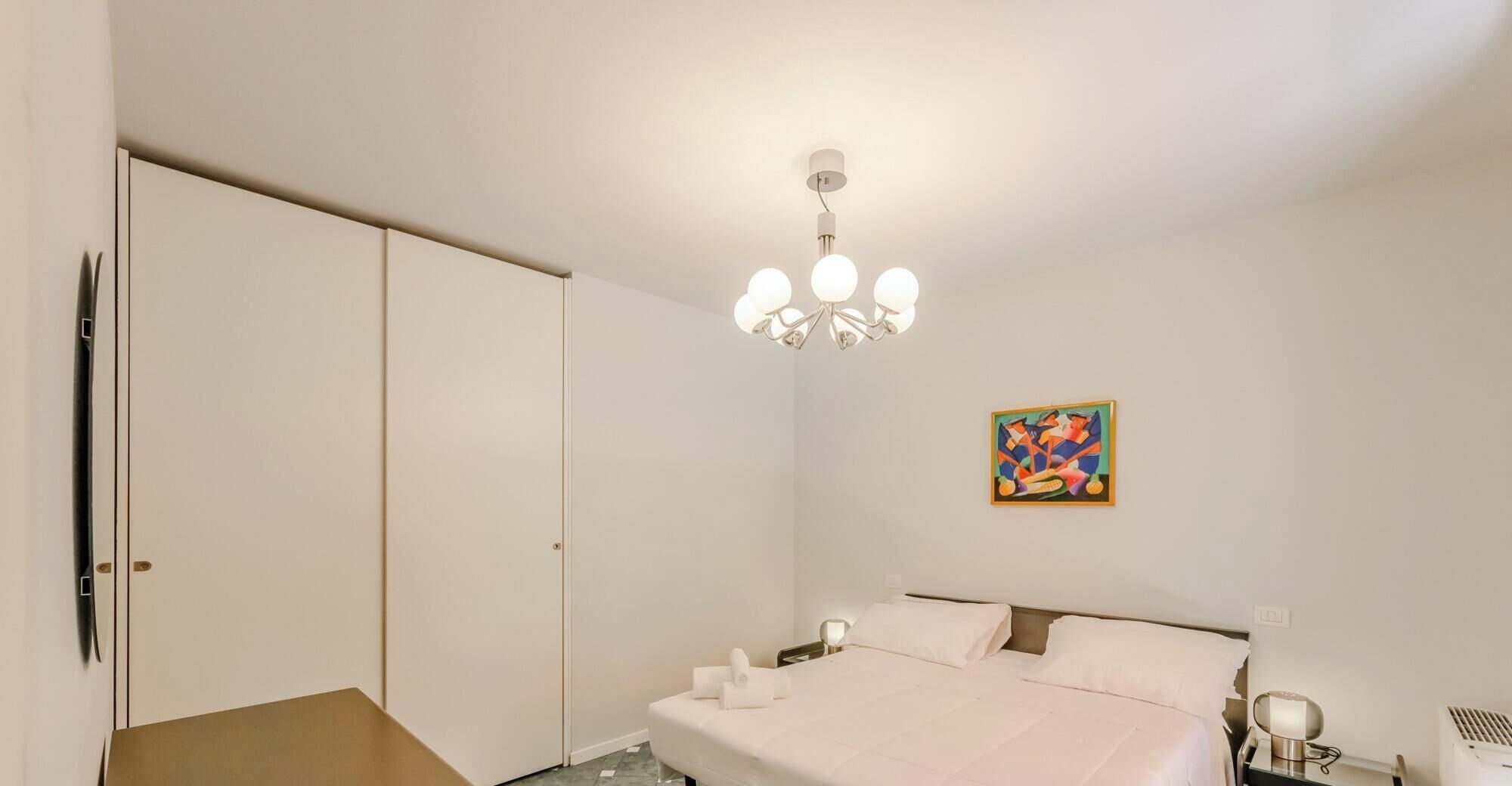 Une chambre à coucher avec un lit, une table de chevet, une lampe, un tableau au mur et une armoire.