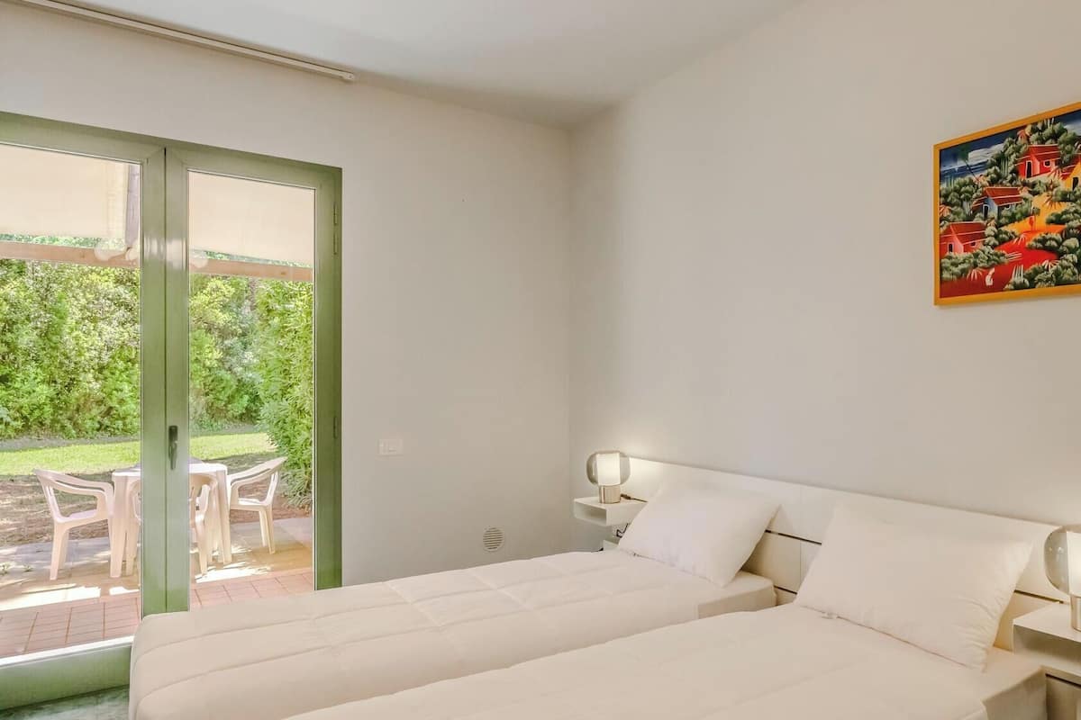 Ein Schlafzimmer mit zwei Betten, einer Schiebetür zu einer Terrasse, einem Nachttisch mit Lampe und einem Bild an der Wand.