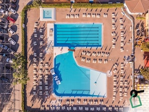 Vue aérienne d’un hôtel avec une piscine, des chaises longues et un parking.