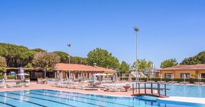 Une piscine entourée de bâtiments aux toits recouverts de tuiles rouges, avec des chaises longues et des parasols à proximité.