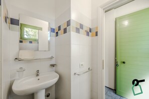 A bathroom with a white sink, a mirror, a toilet, and a green door. - Hotiday Marina di Cecina (Cecina)