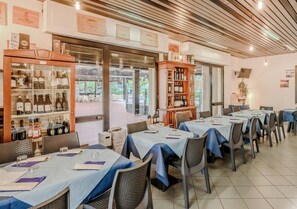 Un restaurant où les tables sont dressées pour le service, avec des présentoirs pour les vins et les spiritueux, et qui offre une vue sur l’espace extérieur aménagé pour les clients.
